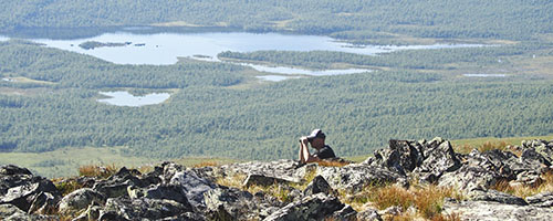En man sitter på toppen av fjället Pieljekaise med en kikare.