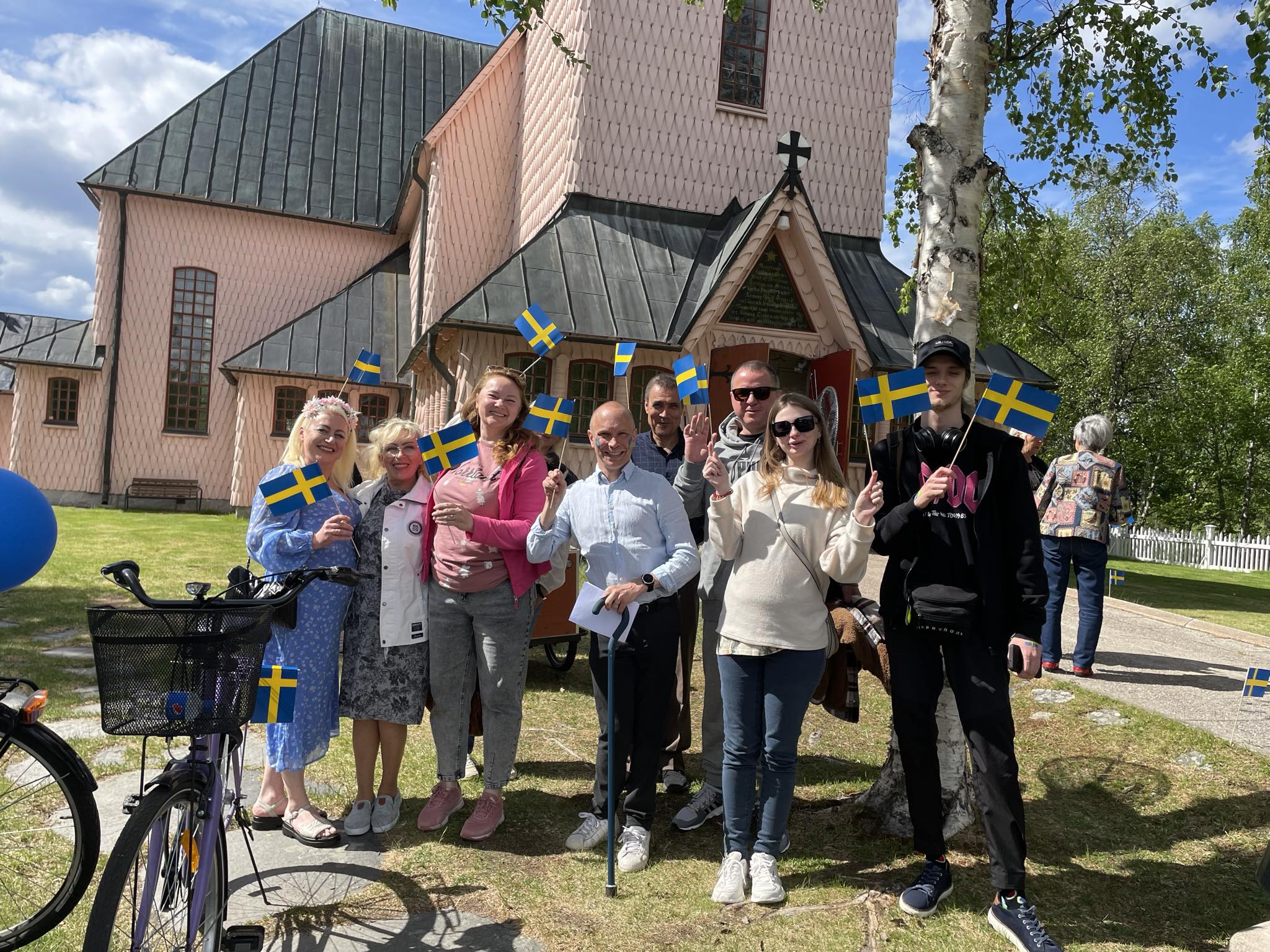 Nya svenska medborgare står framför vår rosa kyrka med sverigevimplar, en vacker sommardag.