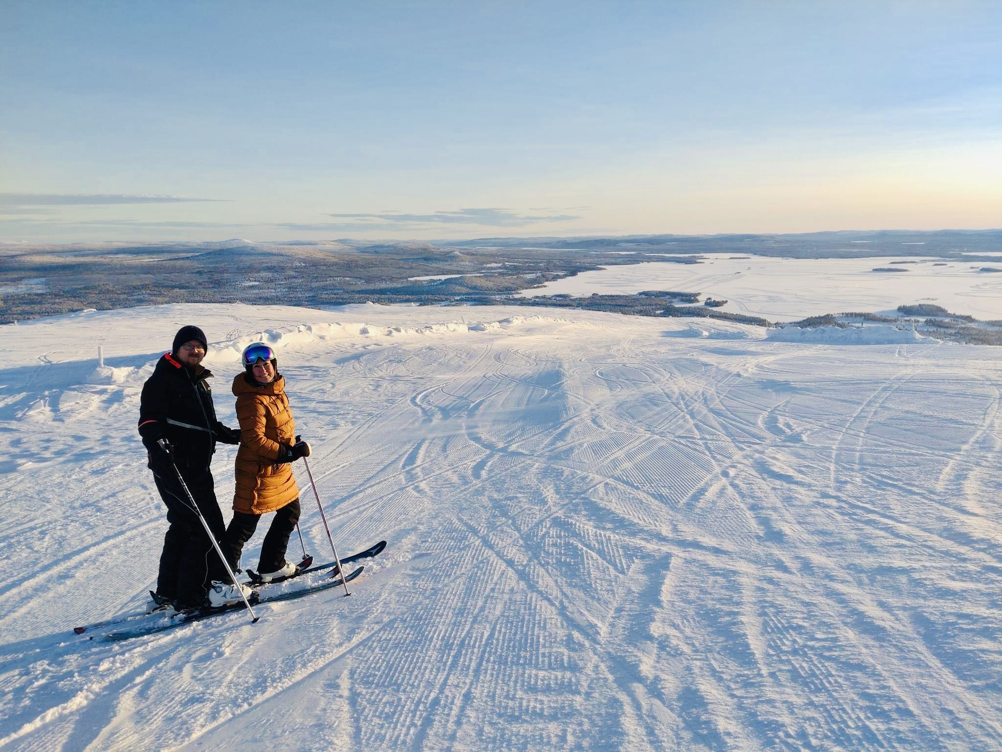 Två människor på toppen av Galtis med Arjeplogs vackra vinterlandskap i bakgrunden.