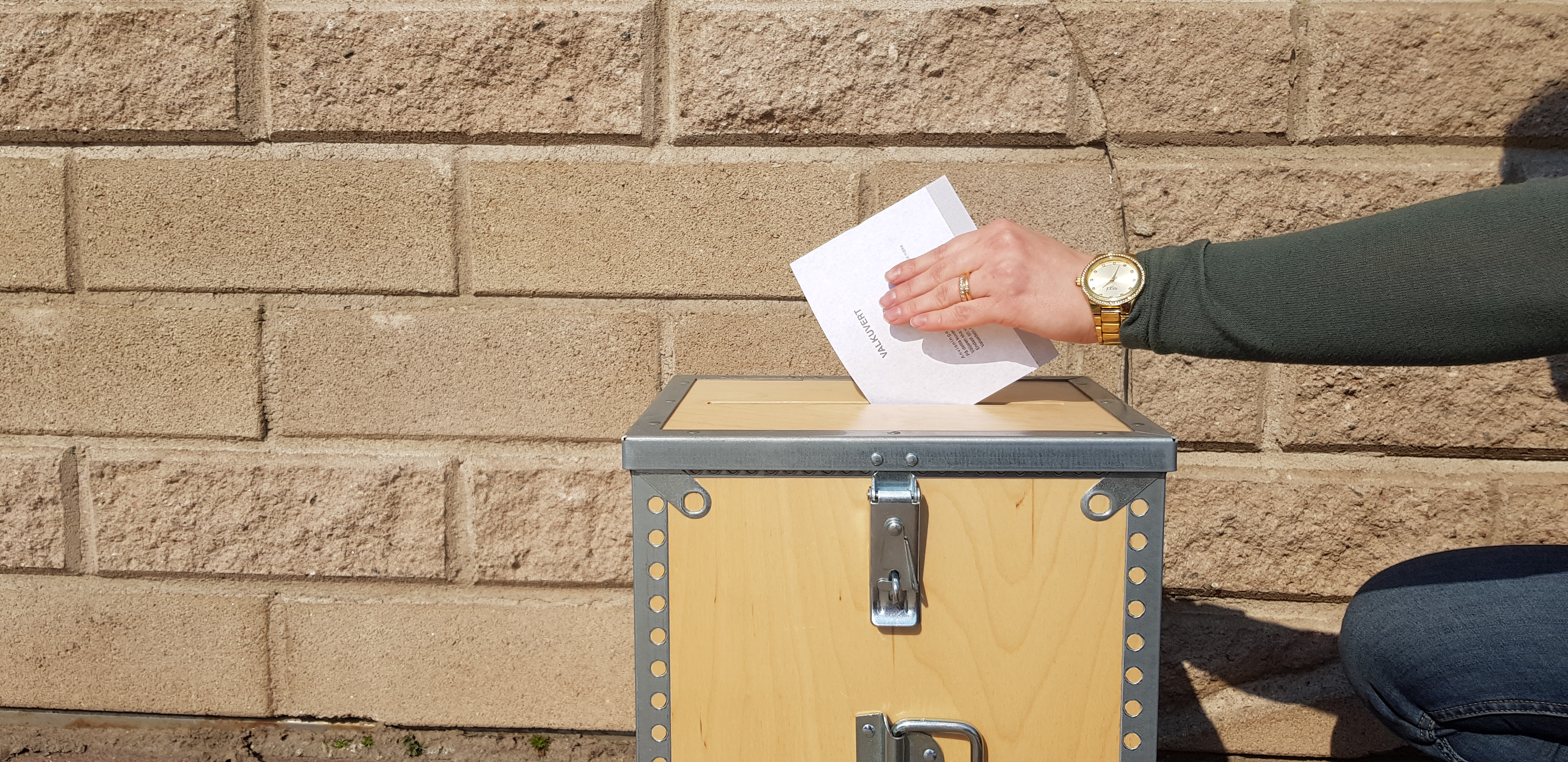 En hand som lägger ned ett röstkort i en valurna, utomhus.