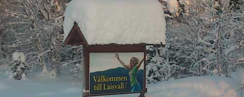 Välkomstskylt till Laisvall, tyngd av snö.
