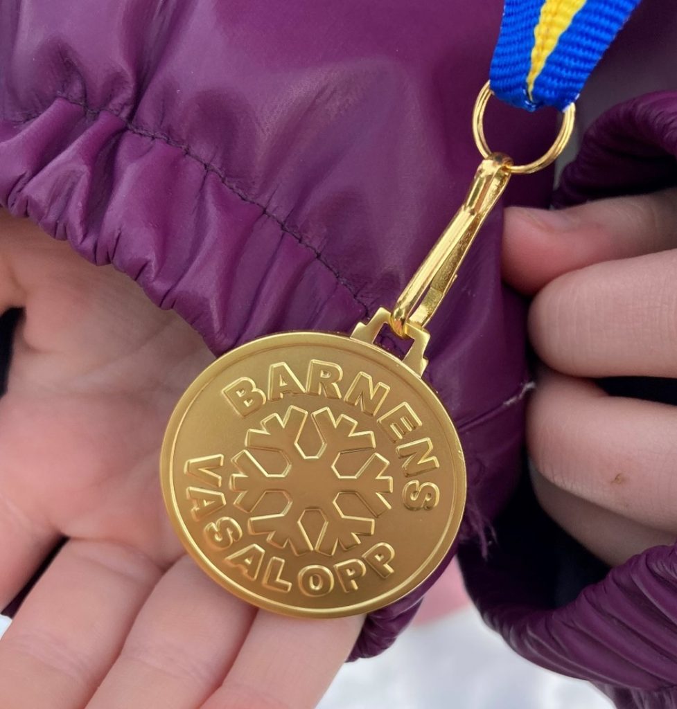 Bild på en barnhand som håller upp medaljen från Lilla Vasaloppet