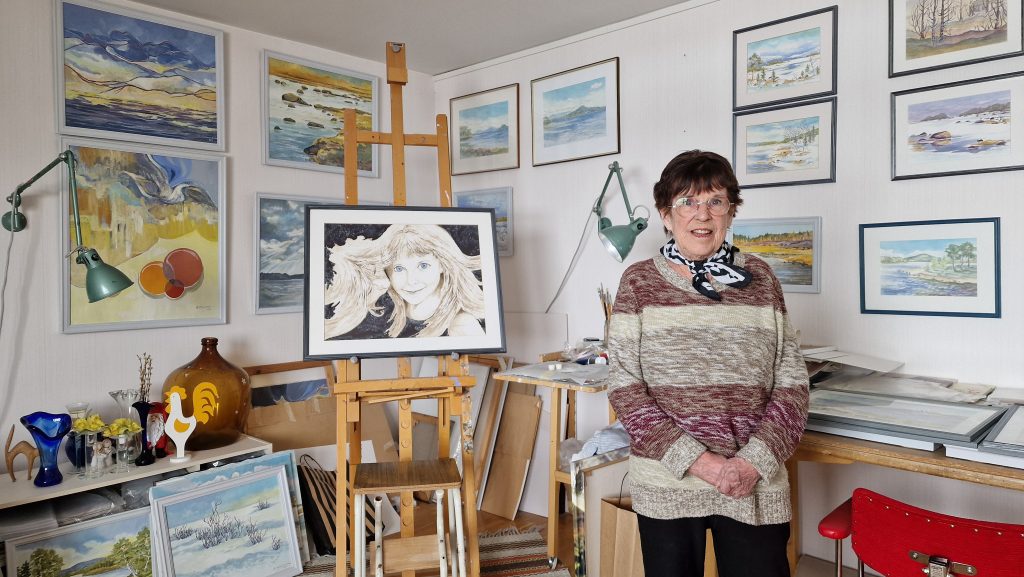 Barbro Holmström, i sitt rum med alla sina tavlor på väggarna.