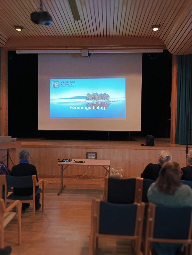 En powerpoint visas på en storduk i Medan. Stolsrader i förgrunden.
