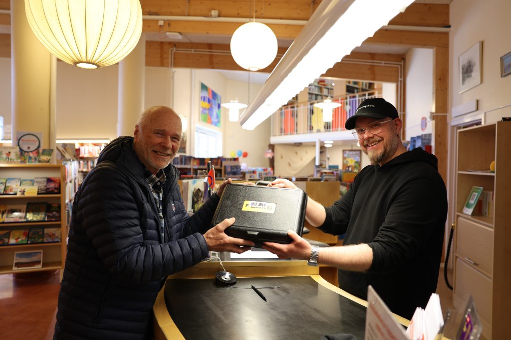 Robert Lidström och Greger Öberg håller i energiväskan, över disken på biblioteket.
