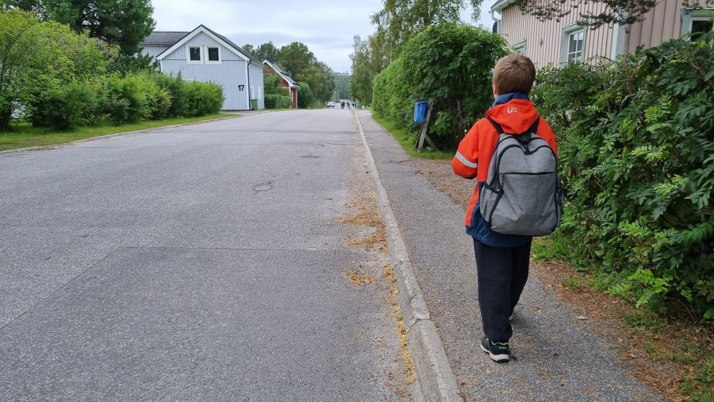 Ett barn som går på en trottoar med en ryggsäck på ryggen.