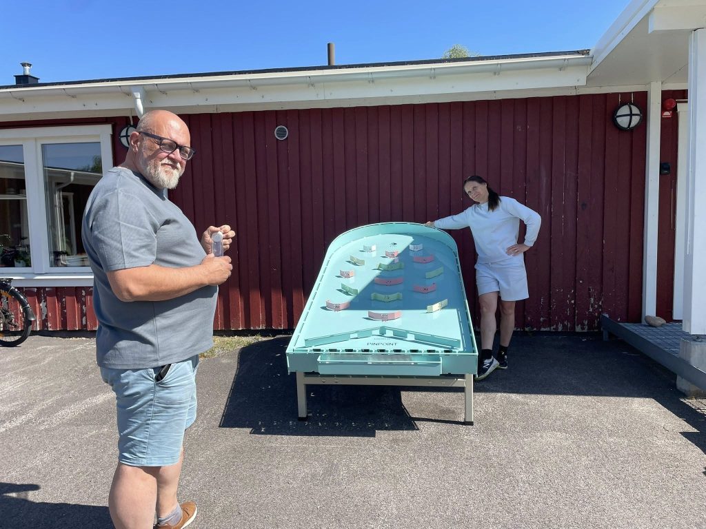 Två personer står vid ett stort utomhus-flipperspel.