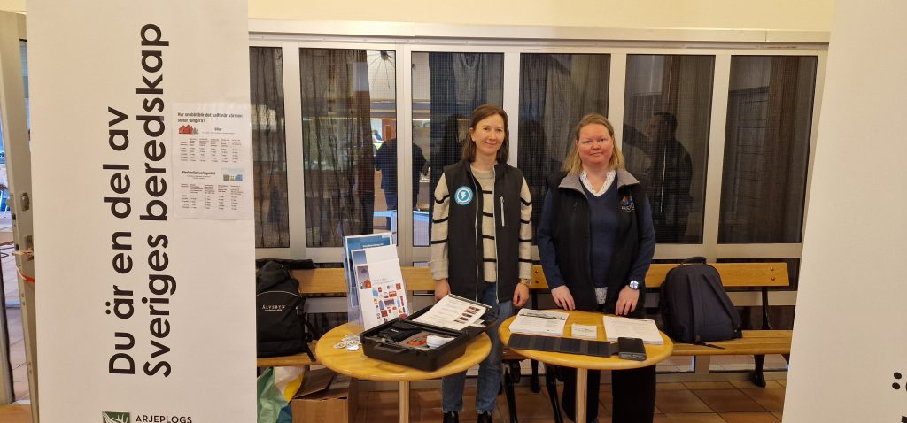 Filippa Ekroth, energi- och klimatrådgivare för Arjeplogs, Arvidsjaurs och Älvsbyns kommuner samt Sandra Ylinenpää, säkerhetssamordnare, står framför ett bord med broschyrer.