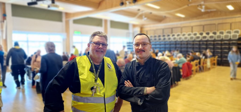 Peter Byrne, kostchef och Isak Utsi, kommunalråd i medan med matgäster i bakgrunden