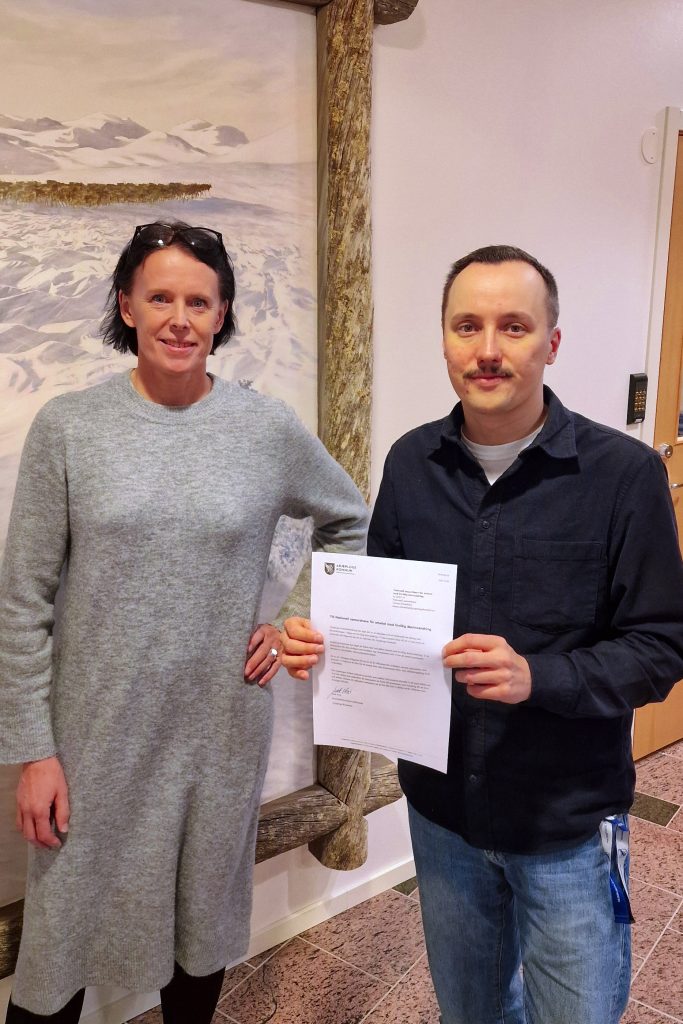 Anna Kaltenegger, kommunchef, och Isak Utsi, kommunalråd, står bredvid varandra. Isak håller i ett papper.