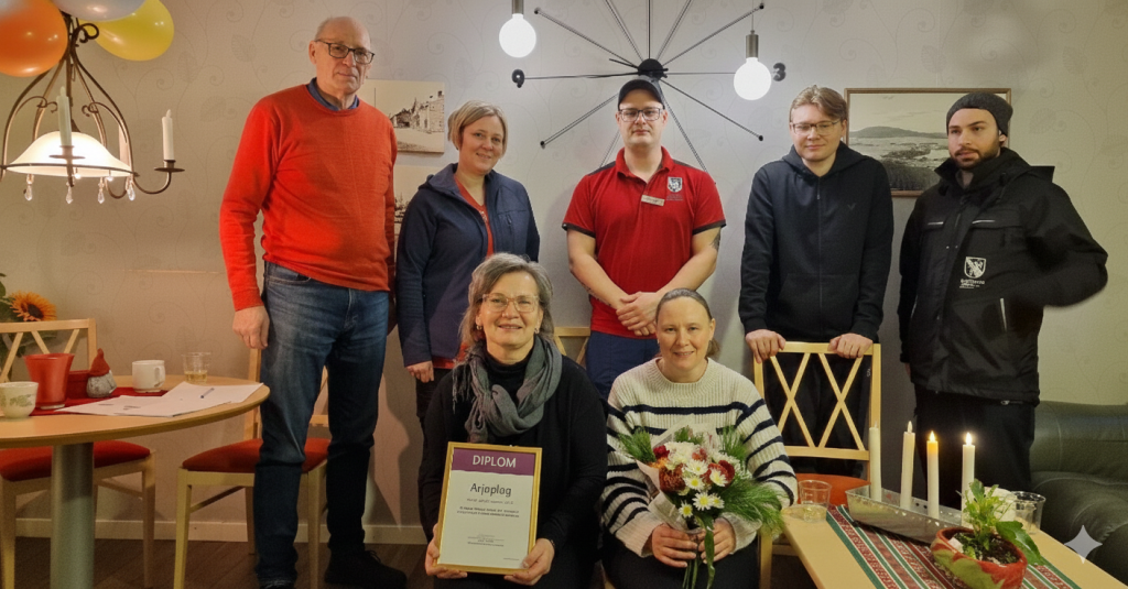 Roland Sellberg står bredvid hemtjänstpersonalen. Enhetscheferna Bitte Westerlund och Carina Juuso står på knä längst fram, med diplom och blommor i sina händer.