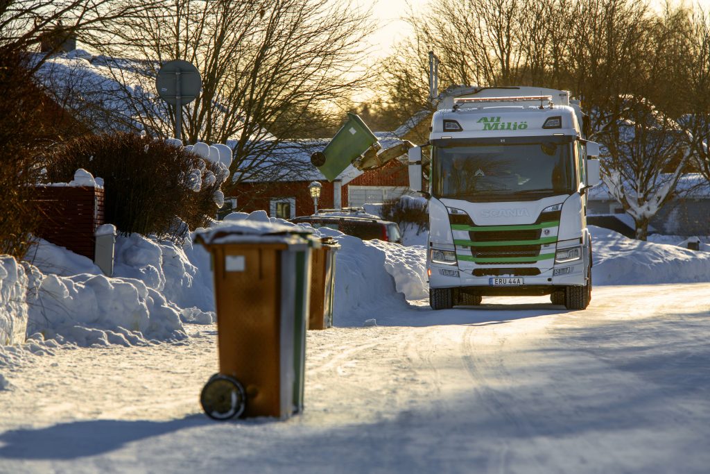 En sopbil tömmer soporna inne på ett samhälle en ljus vinterdag.