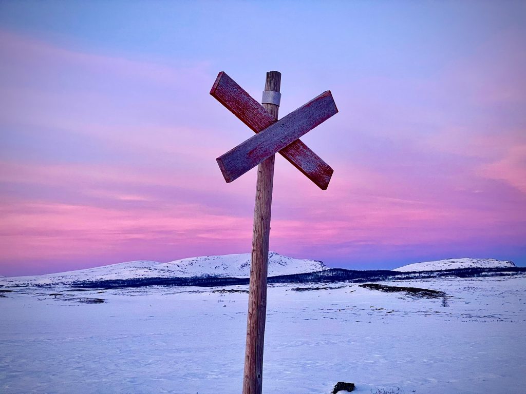 Ett rimfrostat skoterledskryss mot en molnbelupen skymningshimmel.