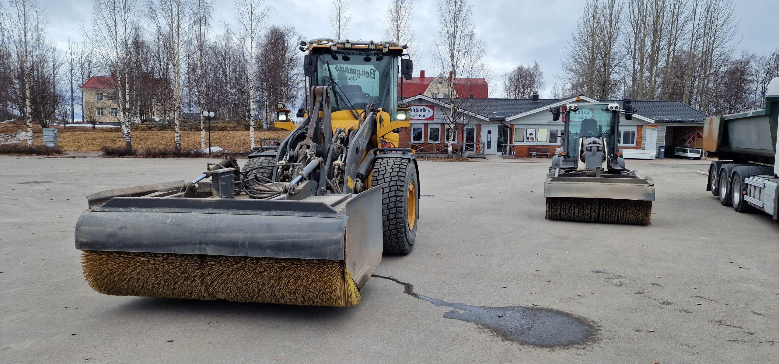 Hjullastare med sopvals för sopning av grus på en parkeringsplats